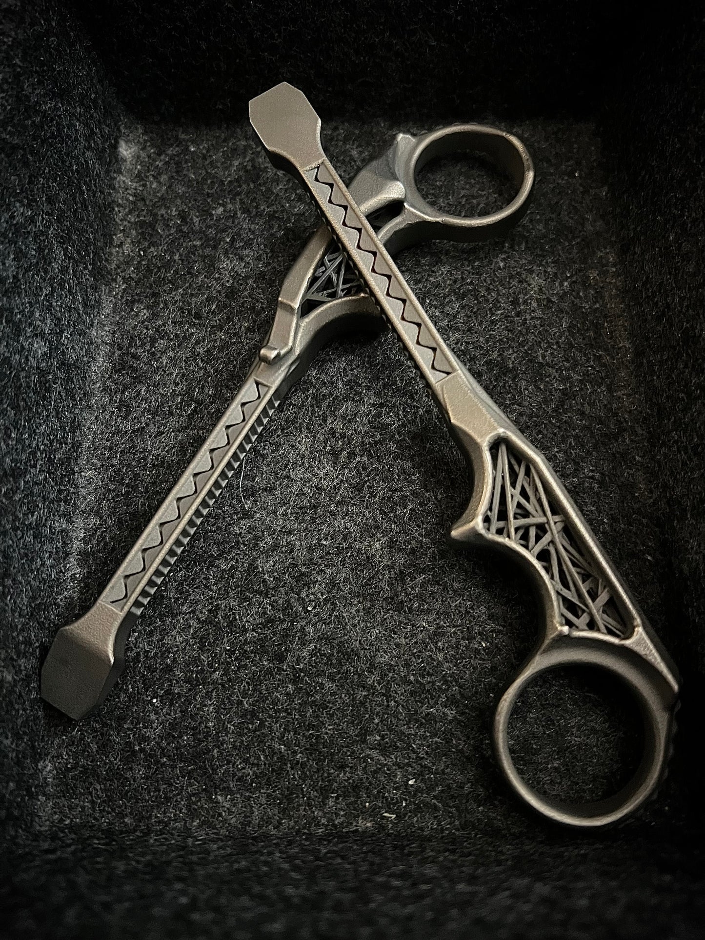 A pair of metallic finger tools with decorative geometric engravings, resting on a dark textured felt surface.