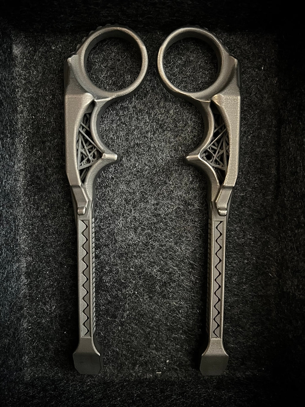 A pair of ornate metal ring scissors with decorative geometric patterns on the handles, displayed on a dark textured background.