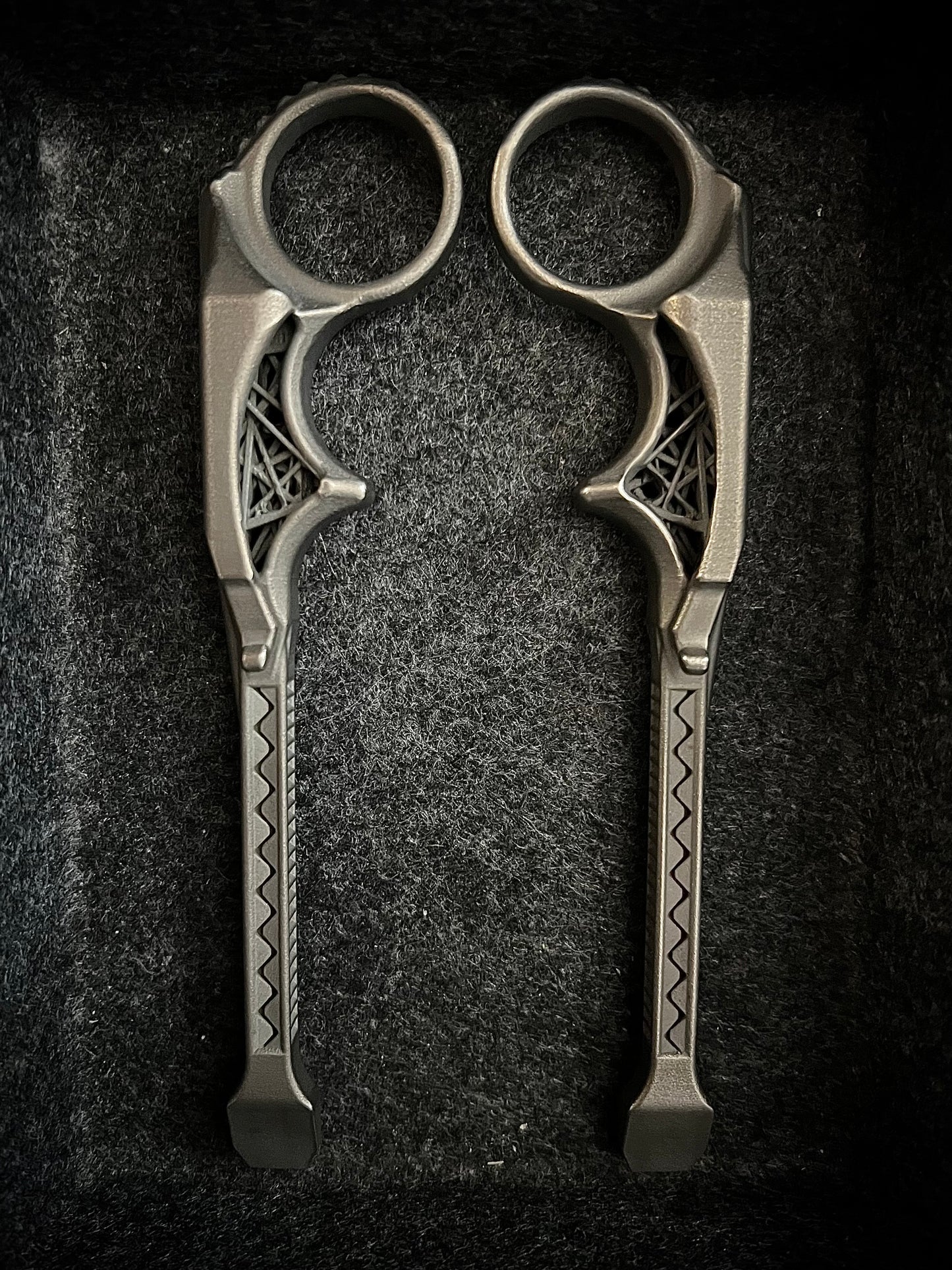 A pair of ornate metal ring scissors with decorative geometric patterns on the handles, displayed on a dark textured background.