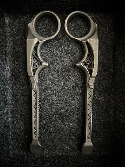 A pair of ornate metal ring scissors with decorative geometric patterns on the handles, displayed on a dark textured background.