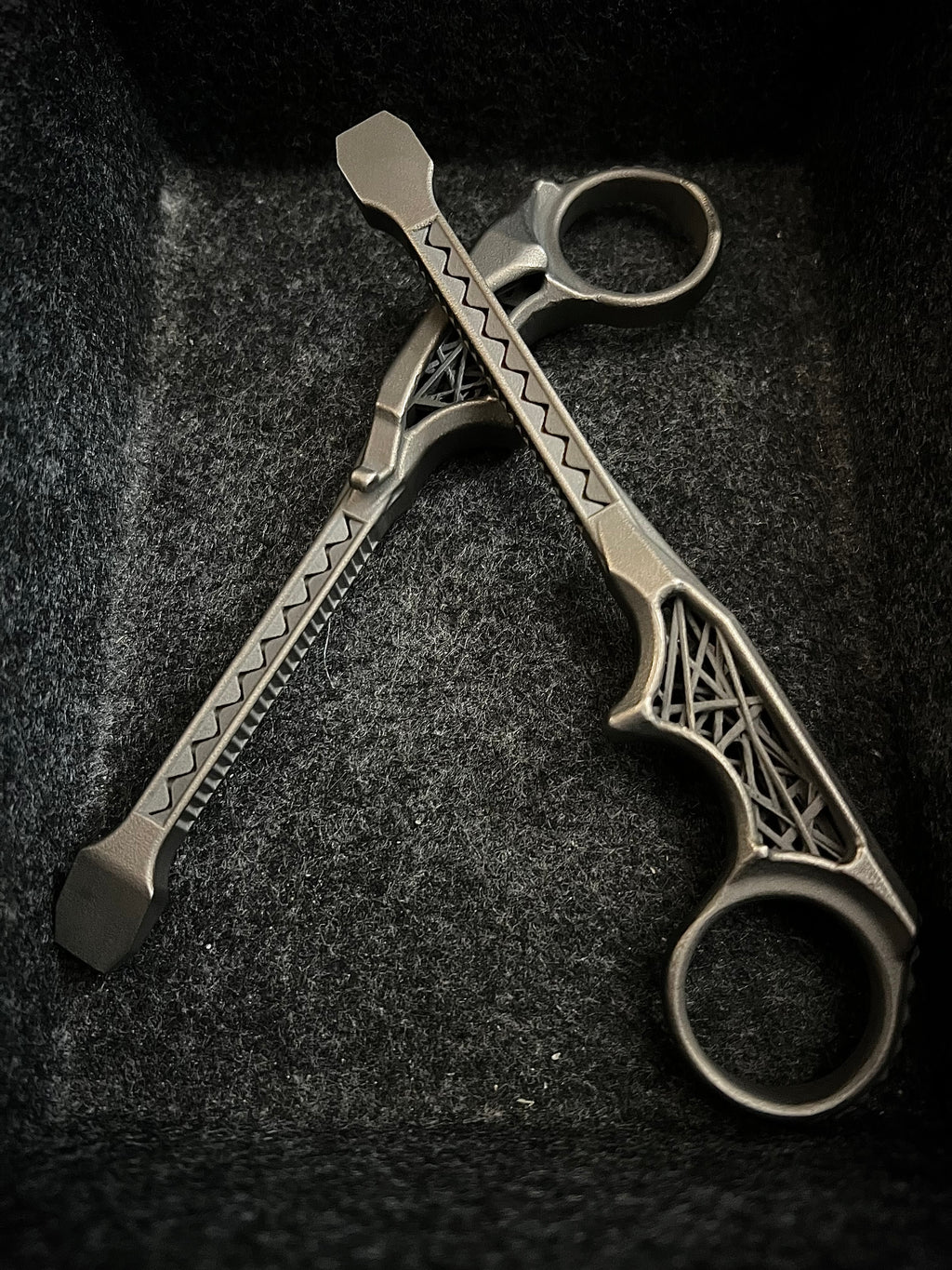 A pair of metallic finger tools with decorative geometric engravings, resting on a dark textured felt surface.