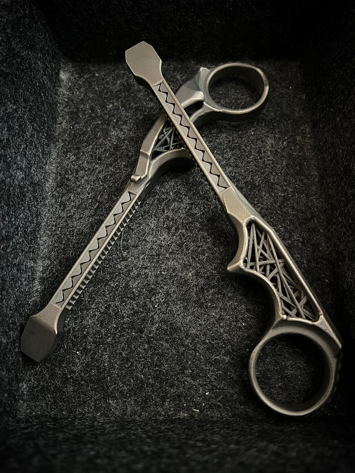 A pair of metallic finger tools with decorative geometric engravings, resting on a dark textured felt surface.