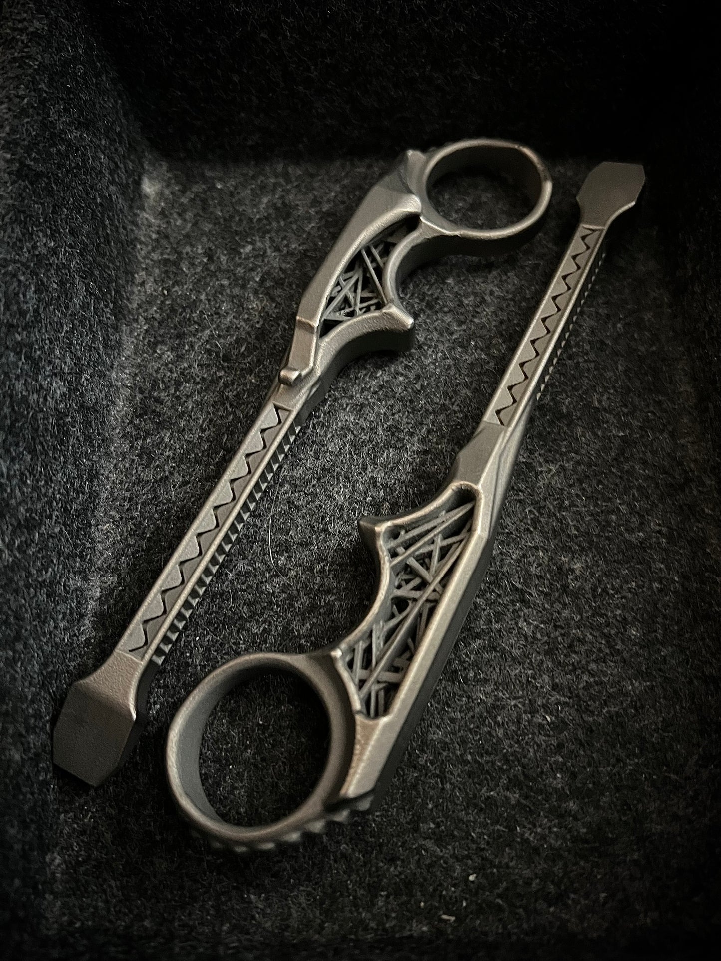 A pair of ornate silver-toned ring scissors with decorative filigree handles, resting on a textured black felt surface.